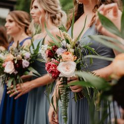 Bridesmaids in blue dresses holding vibrant bouquets during a wedding ceremony.